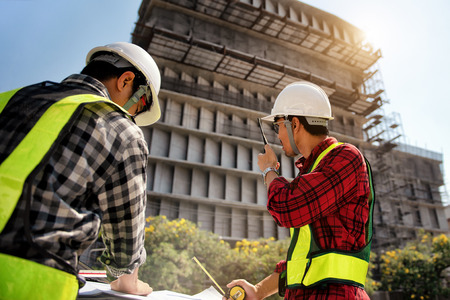 Construction engineers discussion with consultant at construction site or building site of highrise building with blueprintsの写真素材
