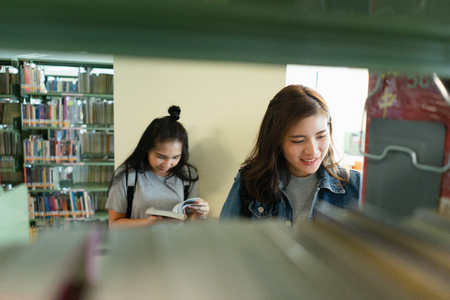 Asian Student searching for textbook in the bookshelf in the International College/University Library. Finding the correct answer to their question preparing for university examination.の写真素材