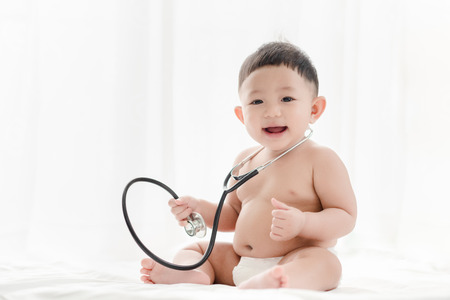 Asian baby boy smiling and plays stethoscope on the bed a white background. Healthcare for Baby and skills develop concept.の写真素材