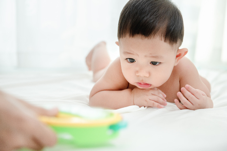 Asian baby boy doubts with colorful toys in mother hand. Baby skills develop concept.の写真素材