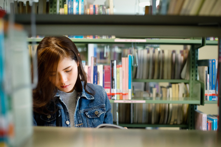 Asian Student searching for textbook in the bookshelf in the International College/University Library. Finding the correct answer to their question preparing for university examination.の写真素材