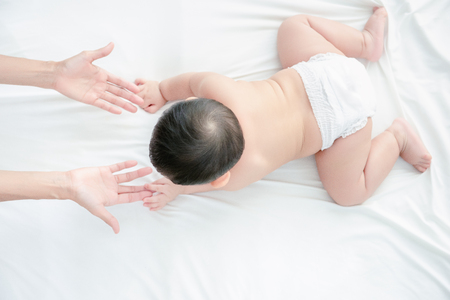 Asian smiling baby boy play and crawling to his mother in living room, Mother extend hand to coming together help baby feel confident. Baby skills develop concept.の写真素材