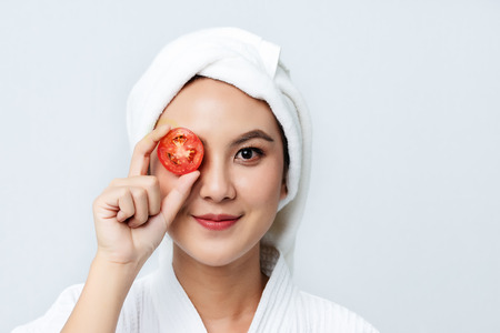 Natural homemade fresh cucumber facial eye pads facial masks. Asian woman holding tomato slices and smile relax with natural homemade.の写真素材
