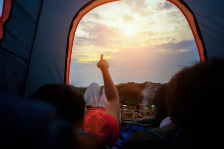 Young woman lying in a tent pointing sky view with sunlight in beautiful time of natural on mountains,  Camping with Sunset in base camp, One Activity Relaxing in summerの写真素材