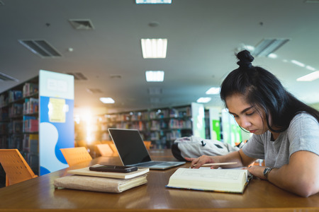 Asian female students learning and making notes writing down information in the library. Learning and preparing for university exam.の写真素材
