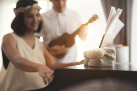 Close-up baby booties with blur background of the Pregnant couple play piano and Ukulele at home with natural warm light. Romantic moments for relationship of pregnant couple. Waiting for baby.の写真素材