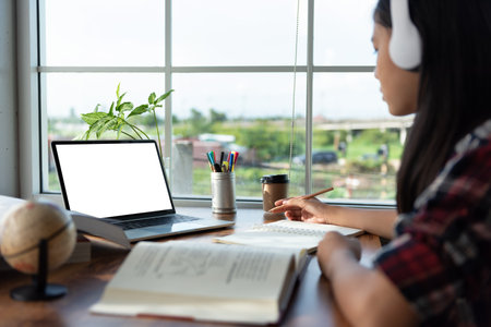 Female student wears headphones and looking to laptop study online and note at home for Studying...