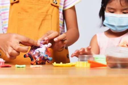 Asian two sisters playing together. Children are doing mold clay to coronavirus imagery while wear...