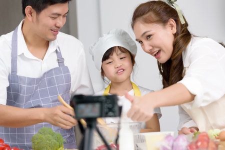 Asian family enjoys cooking together and recording video about tutorial homemade cooking at home kitchen. Person who works freelance on social media broadcasting, Activities together family.の写真素材