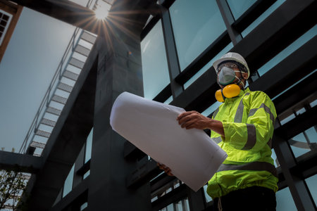 Civil Engineering people wearing face mask and safety helmet on construction site holding blueprint in his hand. Building inspector. Construction site check drawing and business workflow of buildingの写真素材