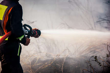Fireman extinguishes a landfill  in harsh conditions of fire, flames and smoke in the background.