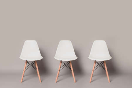 Empty Three Modern White Chair Standing Row on Light Gray Colored Background in Studio with Copy...