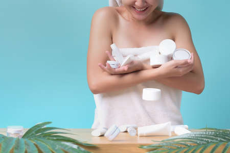 Asian Young woman smile holding packaging of cosmetics and cream product many full hands until fall off down on table on light blue color background with copy space. Concept of Skincare products.の写真素材