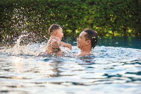 Asian little son enjoys playing in the pool outdoor for the first time with Father, Parent caring for children safe concept.の写真素材