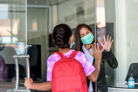 Teachers in medical face mask and raising their hand to greet student girl kids at Tutor school...