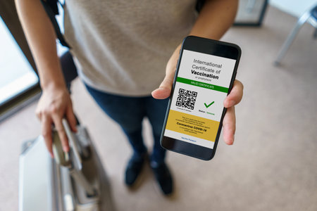 Tourist uses of application on smartphone to show an international certification of vaccination at airport with Immunity passport and vaccination record card , Disease immunity passport.の写真素材