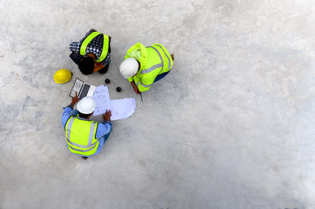 Civil engineers consider with construction foreman while looking at blueprint and schedule target on a laptop at construction site in morning time before work startup. Top view with copy space.の写真素材