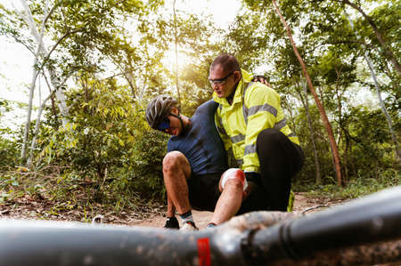 Cyclist accident falling off mountain bike and knee injury and first aid at MTB track. Athlete...