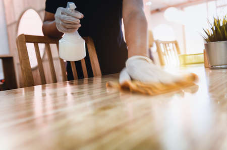 Hand of waiter woman cleaning table with disinfectant spray and microfiber cloth for disinfecting at indoor restaurant. Add movement filter effect. Coronavirus prevention concept.の写真素材
