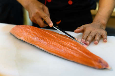 Fresh salmon fillet close-up on white cutting board table while filleting salmon belly by chef in cooking room. Selection focusing on salmon fillet with Soft focusing shooting.の写真素材