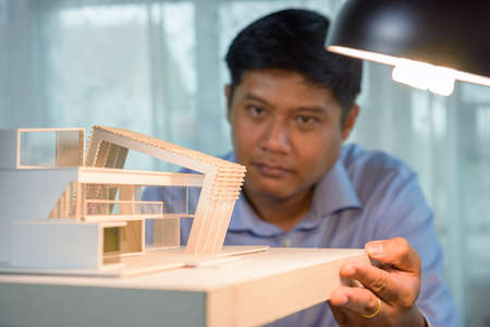 Architect-designer holding model of modern box house while thinking about concept of building and construction project before startup in the future. Focusing on modern box house model.の写真素材