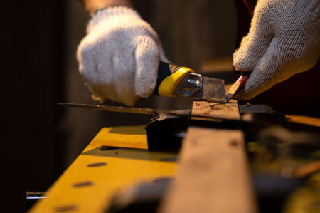 Close-up of Carpenter hands use old sharp Utility knife for manual sharpener pencil with fabric glove in warm light workshop, Using snap blade knife to sharpen pencil equipment for marking in workの写真素材
