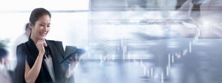 Asian businesswoman uses technology tablet looking to profit and stock trading signals in stock markets, Communicate with brokers trading, Buy and Sell background with copy space in bannerの写真素材