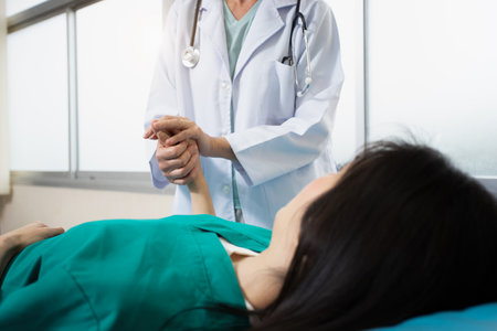 One patient female wearing green patient gown look like diseased not feeling well laying down in front of doctor with stethoscope and white coat holding hand for give motivation and cure sicknessの写真素材