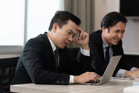Asian businessman frowning with stressed only one during meeting at conference room. Businesspeople nervous and feeling more tired in job, Migraine, Physical health is not ready to work.の写真素材