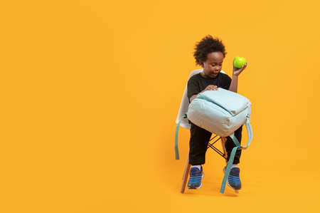 Black child boy 3 years, Students kid with school bag sitting complain own while hold a green apple, Isolated portrait on yellow background with copy spaceの写真素材