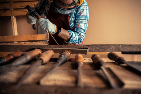 Carpenter wearing brown apron use an old chisel with a hammer to carve a wooden in workshop, ...