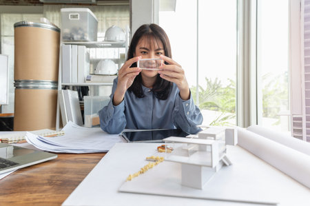 Professional architect women working in designer jobs while holding something part of modern house model on desk having blueprint, material sample and tablet at loft office.の写真素材