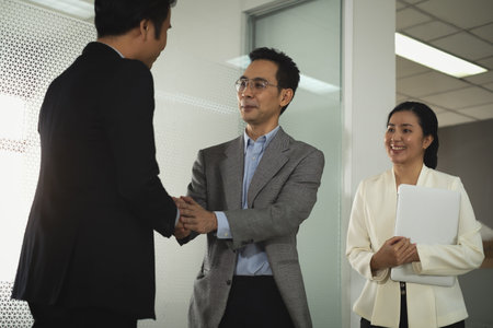 Businessman in smart office suit shaking their hands with partners and secretary after successfully negotiated business together at front of meeting room unclear mirror wall.の写真素材