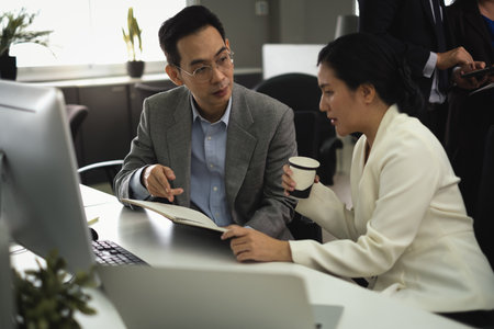 Management people explain to office employees women about job project in daily notebook and point his finger in an office work area.の写真素材