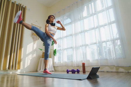 Fitness course at home with Technology tablet online, Asian female in sportswear and sneakers exercising indoors to burn fat doing raise your feet and balance, making body strong. Healthy lifestyle.の写真素材