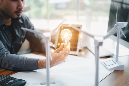 Energy engineer holding light bulb in modern office with solar cell sample and wind turbine model, Creative thinking innovative alternative energy design. Saving nature or ecology concept.の写真素材