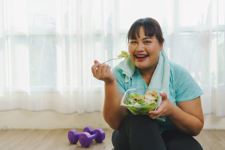 Fitness and Healthy food concept. Portrait Asian women plus size body in sportswear looking camera while smiling enjoys fitness and happy in eating healthy food after exercising at home.の写真素材