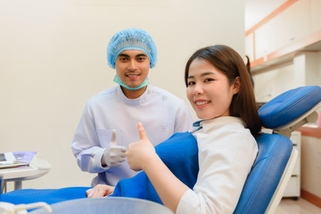 Dentist young Indian and Asian patient looking camera while thumb up to excellently in dental clinicの写真素材