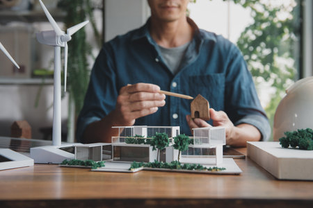 Architect designer making modern home office model for living using natural energy concept, natural light and green tree around, with wind turbine model and solar panels. Focus shoot at home model.の写真素材