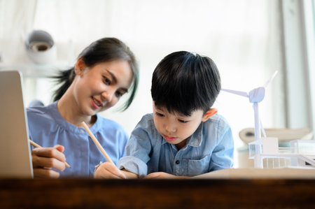Little kid son practicing pencil drawing and writing under mother's control, While Young Asian...