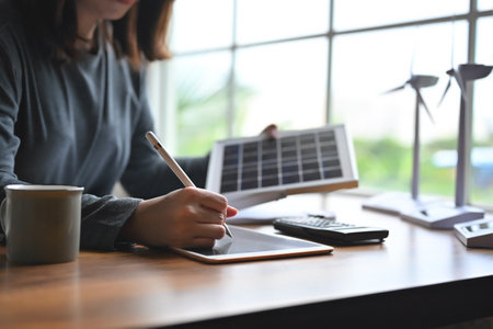 Alternative energy engineers use technology tablet on table for learning design and calculation for energy accumulation in photovoltaic panels installed while holding solar panels samples in hand.の写真素材