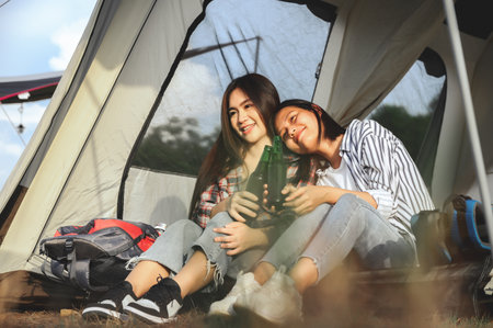 Asian couple women, LGBTQ teen couples travel sitting together drinks in camping tent evening time in a romantic nature atmosphere. LGBTQ lesbians, Lesbians girlfriend, Best friend.の写真素材