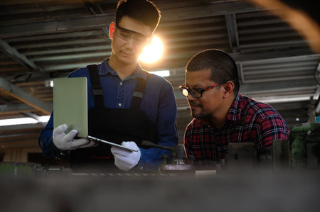 Asian apprentice young engineer discussion with a technician on the job while holding a laptop in...