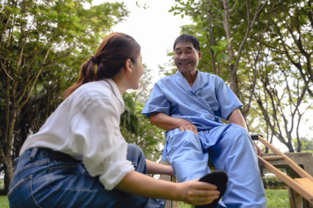 Daughter takes care to foot massage her father, Encourage him during his illness in hospital garden. The happiness of old adult patients while rehabilitation or physical therapy of retired patients.の写真素材