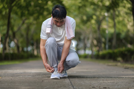 An Elderly Asian Man Is Tying Shoelaces In The Park Full Of Trees Prepare Jogging Or Exercise.の写真素材