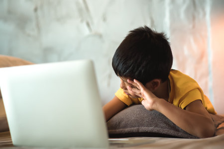 Tired and sleepy of learning or school homework for children. Asian boy students are bored during online education on a laptop in bed at home and falling asleep while studying.の写真素材