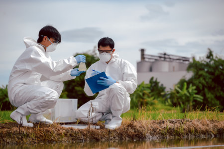 Factory scientists or biologists wear protective clothing while Collecting water samples in natural water sources near farmland. Concept of Chemical protection may leak into natural water sources.の写真素材