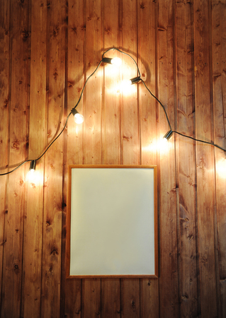 Frame with empty free place for design on a wooden wall with retro garland of glowing bulbs. Christmas moodの写真素材