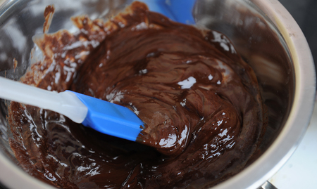 Chocolate and butter melt in a water bath. Blue silicone spatula. The process of making the dessert or sweets. Closeupの写真素材
