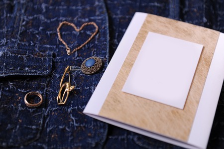 Gold jewelry and certificate with empty blank for design on a blue denim background. Ring, brooch in the form of cat, bracelet chain lies like heart.の写真素材
